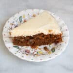 A fluffy piece of gluten free carrot cake on a plate topped with cream cheese icing.