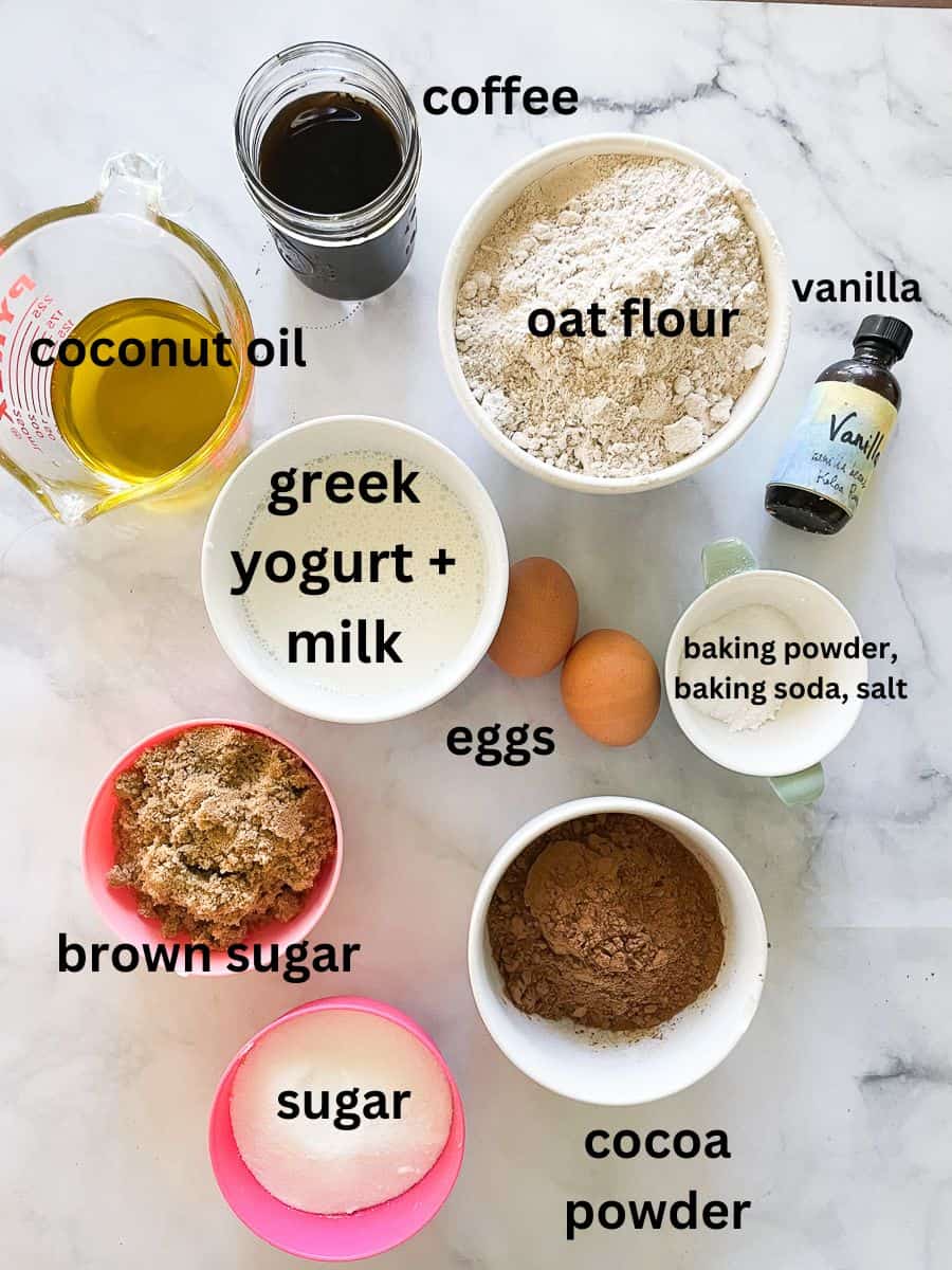 The ingredients for gluten free chocolate cupcakes are shown: cocoa powder, sugar, brown sugar, baking powder, baking soda, salt, coffee, eggs, greek yogurt, milk, vanilla.