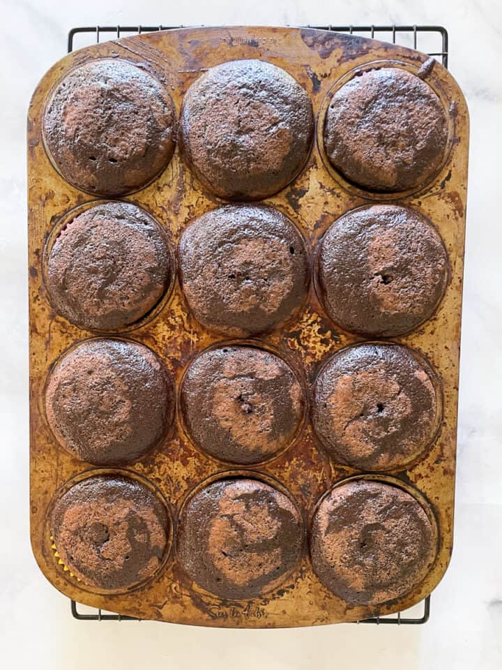 One dozen baked gluten free chocolate cupcakes in a tin.