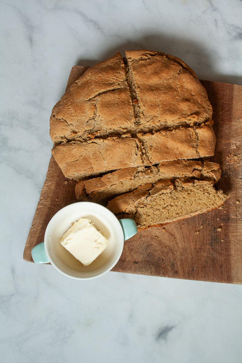 A loaf of gluten free soda bread on a cutting board with a little bowl of butter.