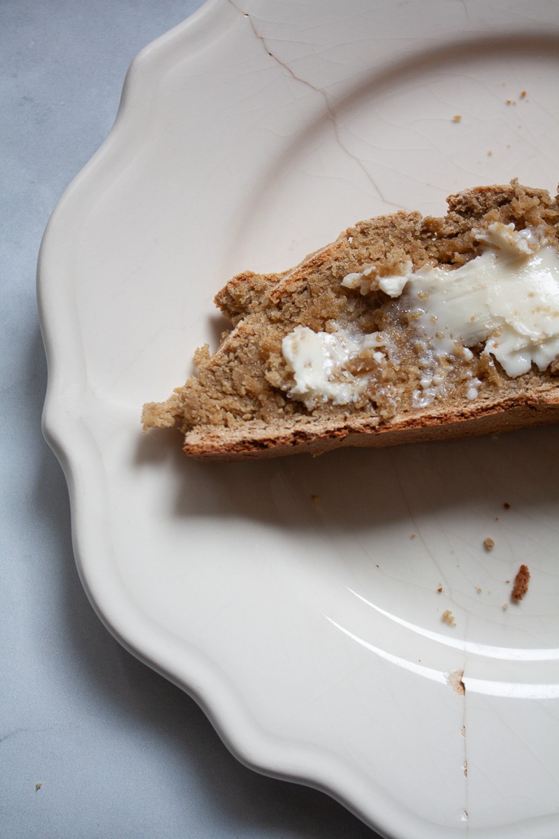 A side view of a piece of gluten free soda bread and butter on a plate.