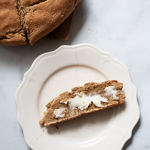 A loaf of gluten free soda bread and a slice of bread and butter on a plate.