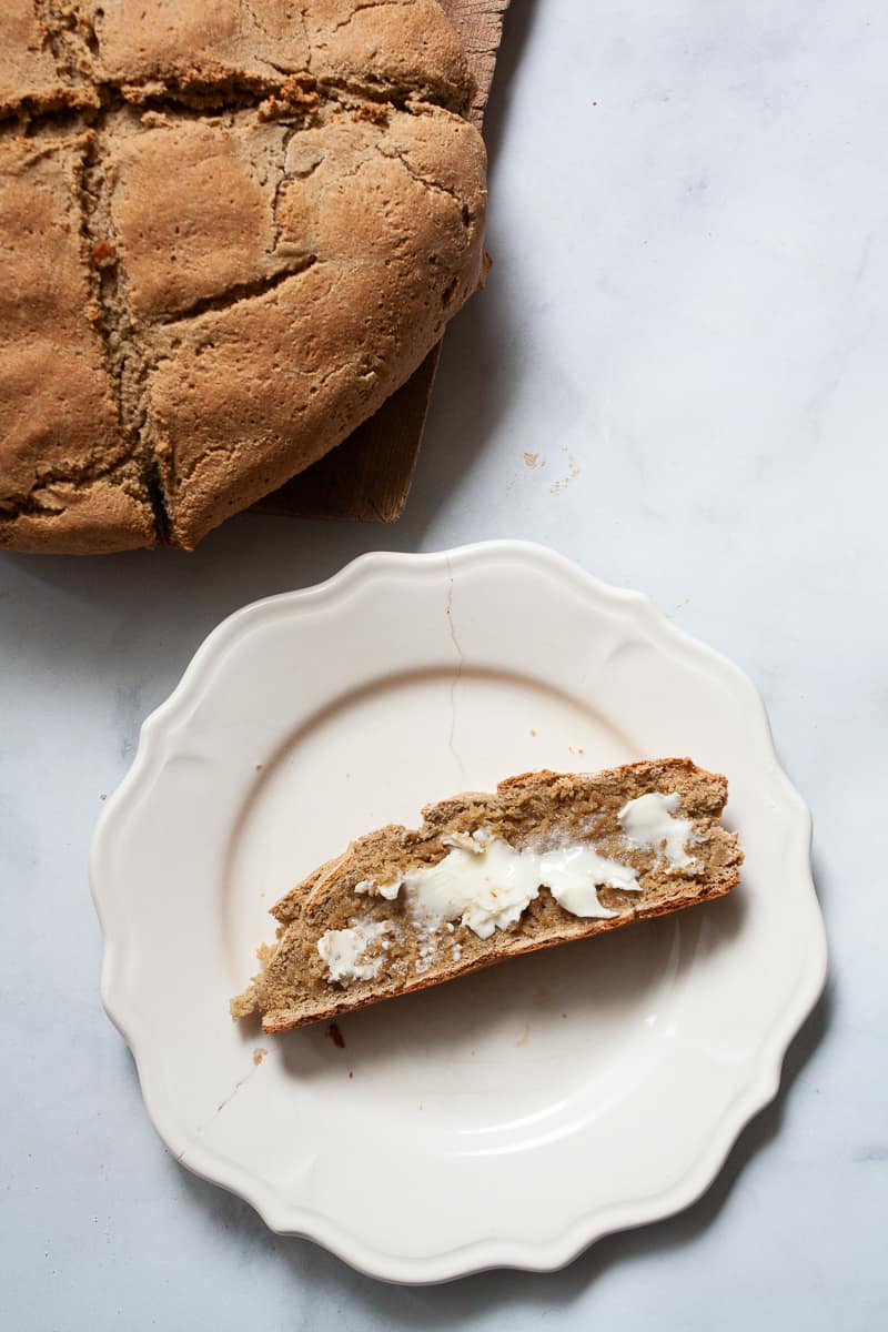 A loaf of gluten free soda bread and a slice of bread and butter on a plate.