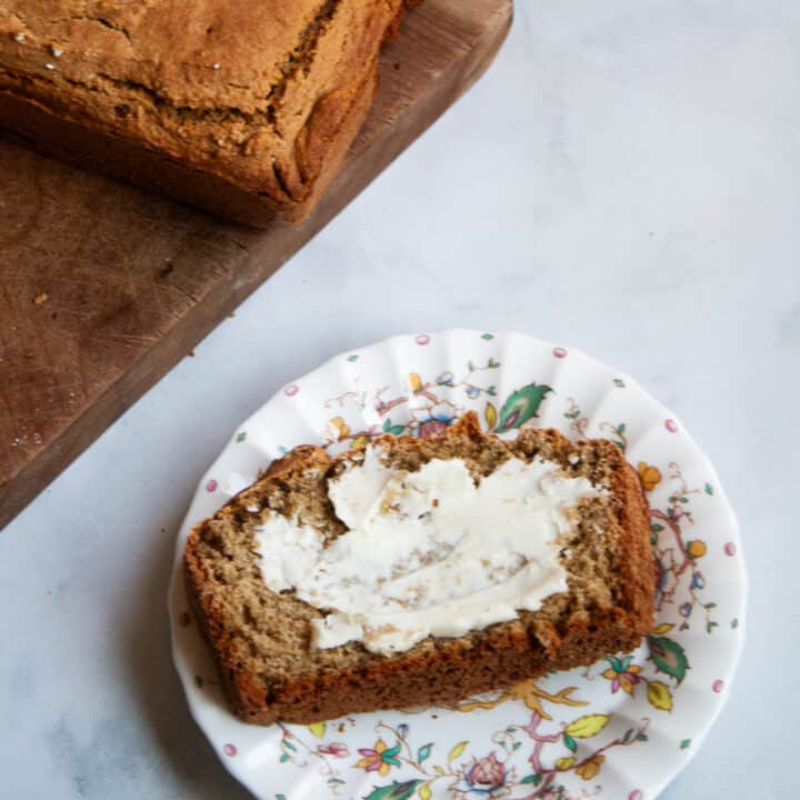 A piece of gluten free Irish soda bread with butter on a plate with the loaf nearby.