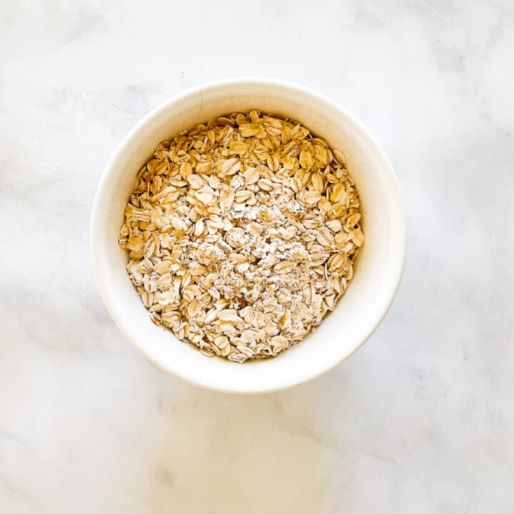 A white bowl holds oats on a marble background.