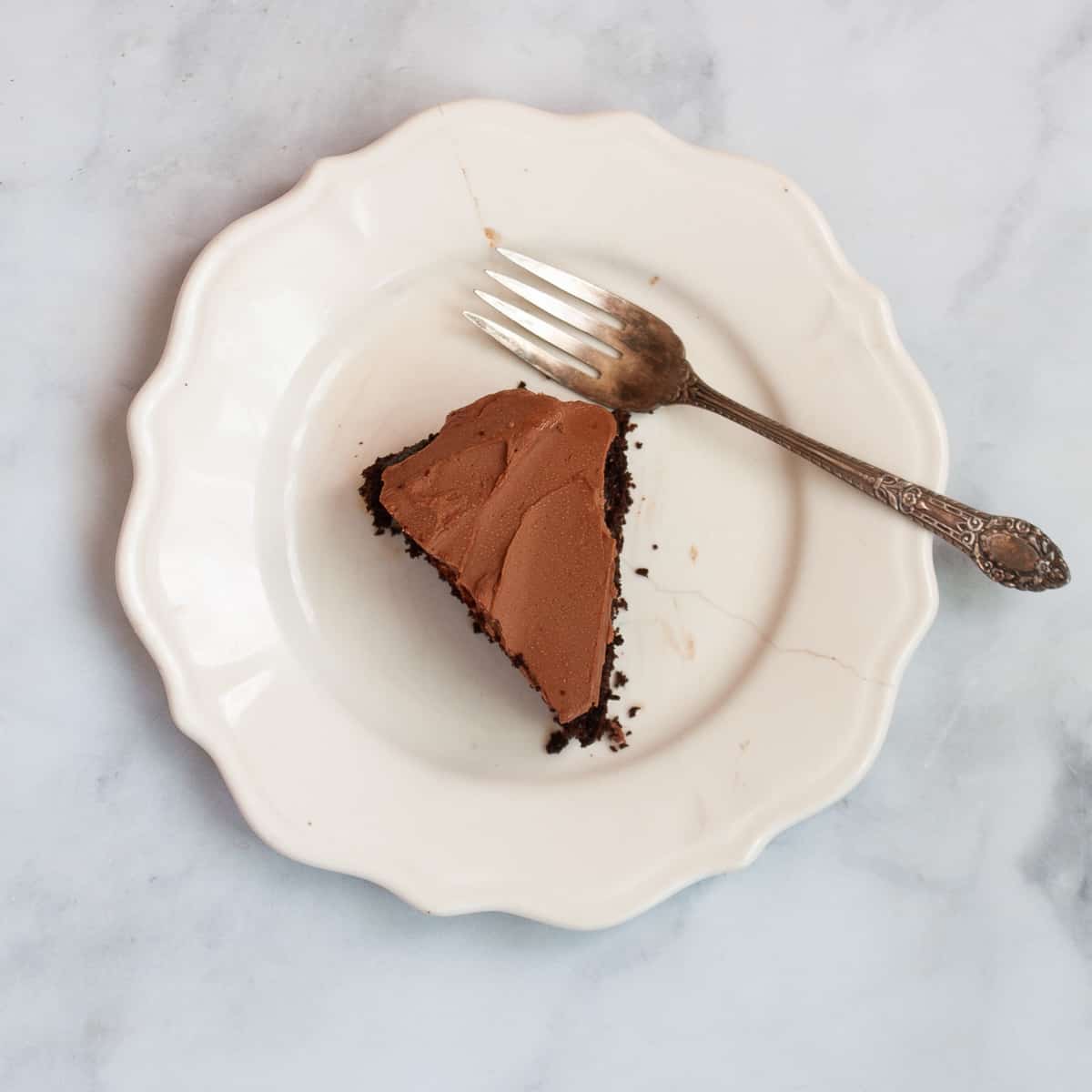 A white plate holds a slice of oat flour chocolate cake with a fork alongside.