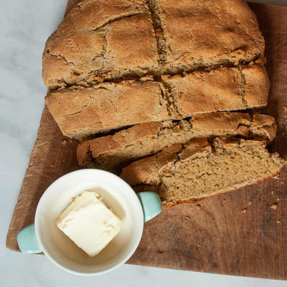 A loaf of gluten free soda bread on a cutting board with a little bowl of butter.