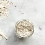 A jar of homemade gluten free flour blend on a white background.