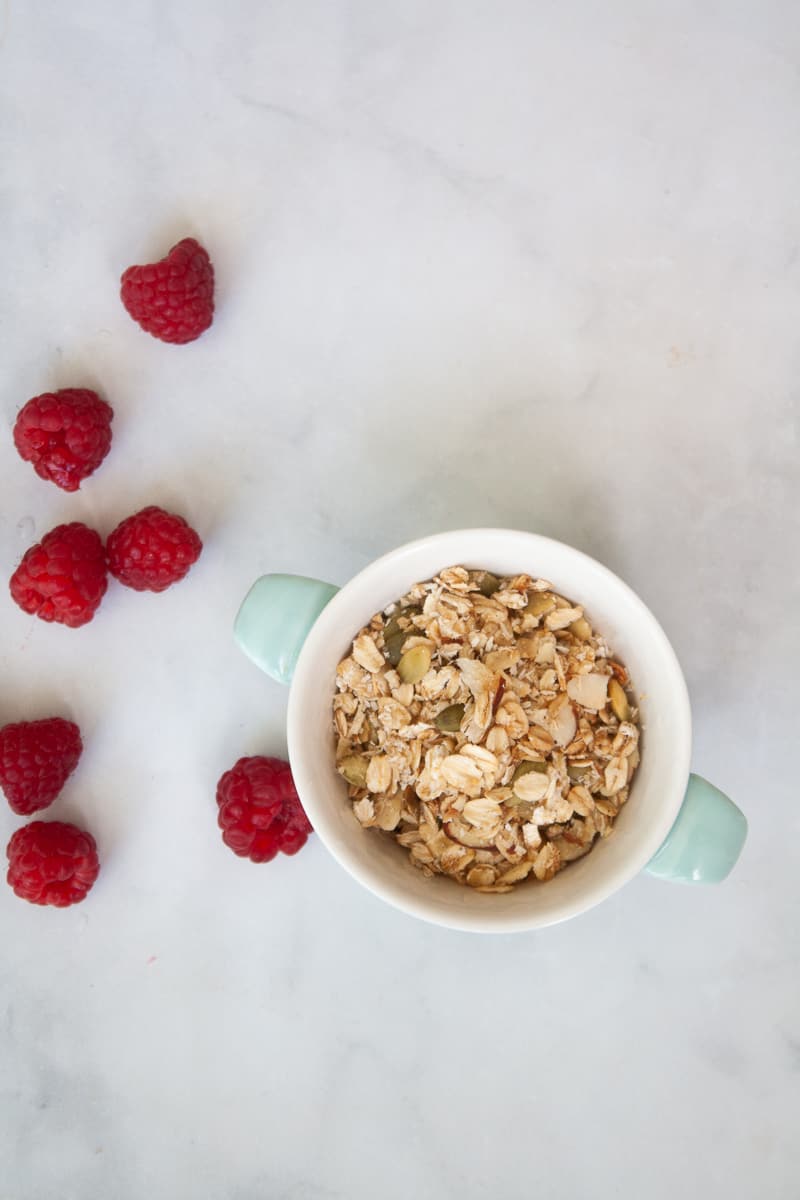 A bowl of gluten-free granola with raspberries scattered around it.
