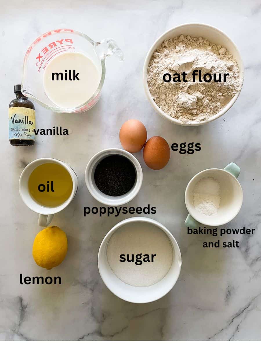 Ingredients for gluten free lemon and poppyseed cake are shown: milk, oat flour, sugar, lemon, poppyseeds, oil, vanilla.