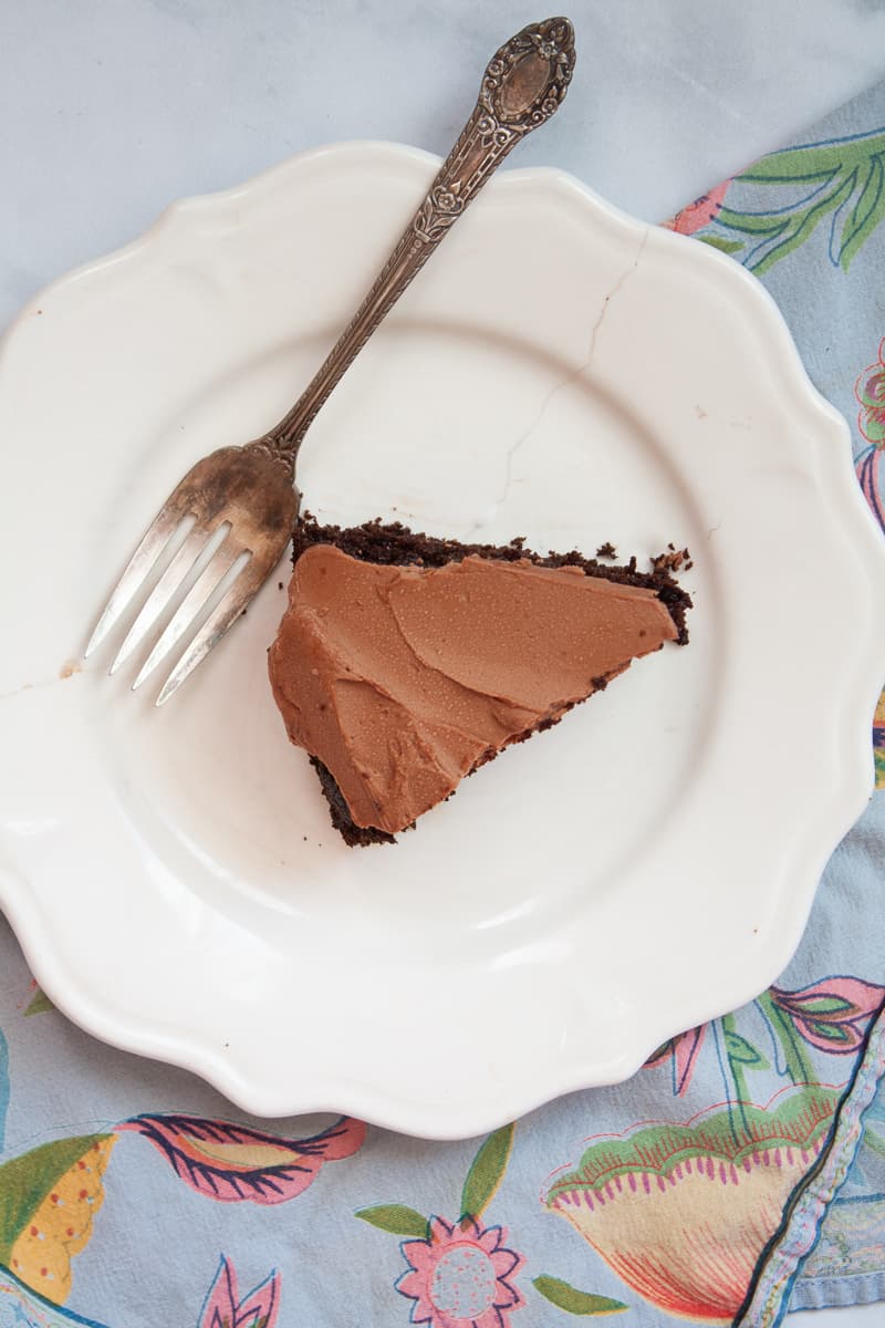 A piece of oat flour chocolate cake on a white plate placed on a blue napkin.