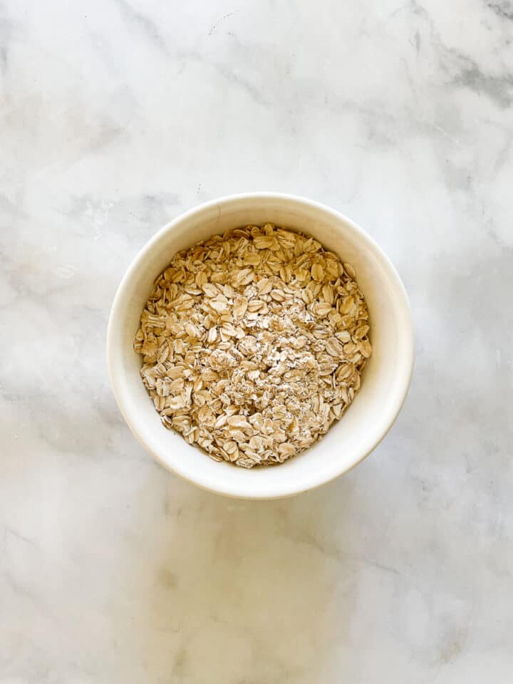A white bowl holds oats on a marble background to answer the question, are oats gluten free.