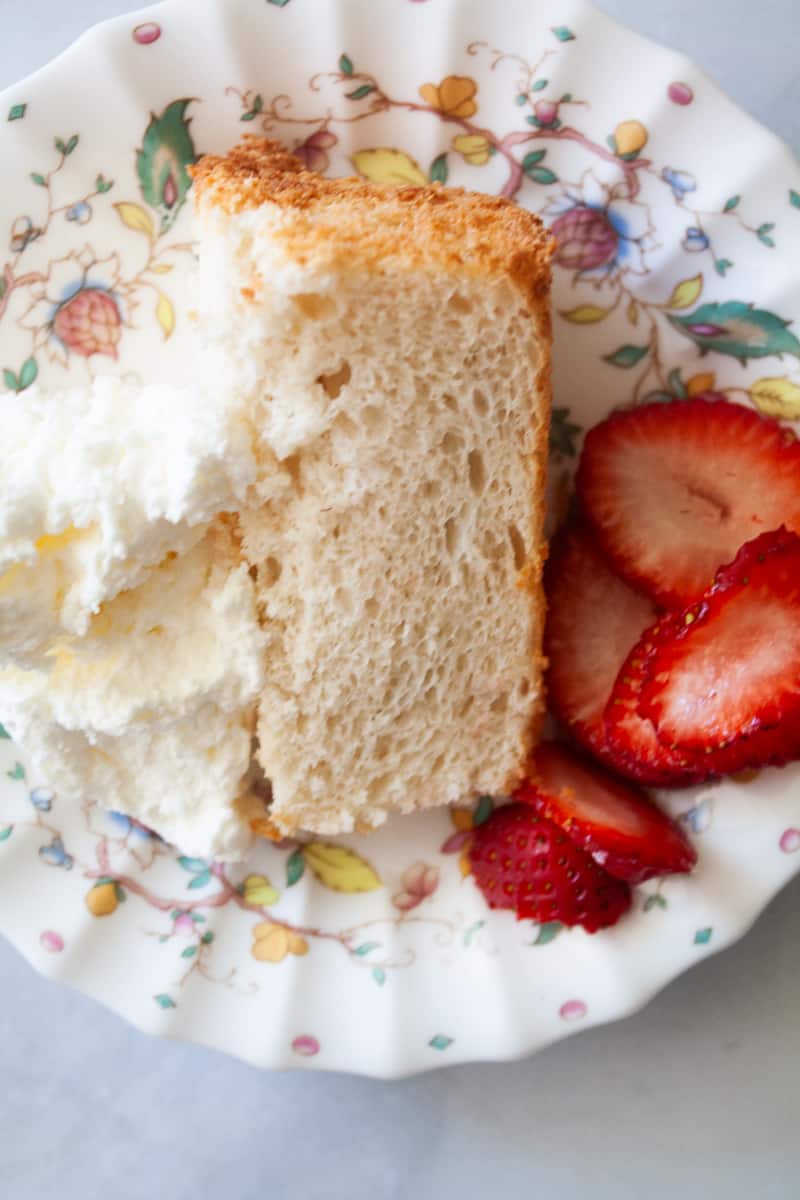 Whipped cream tops a slice of angel food cake on a plate.