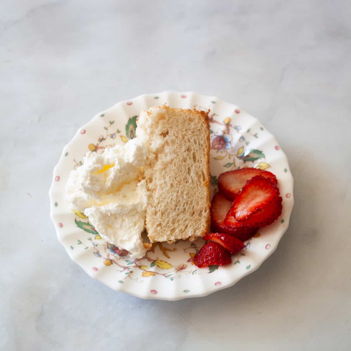 A slice of gluten free angel food cake with sliced strawberries and whipped cream.