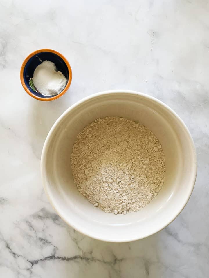 A bowl of oat flour with baking soda and salt next to it.