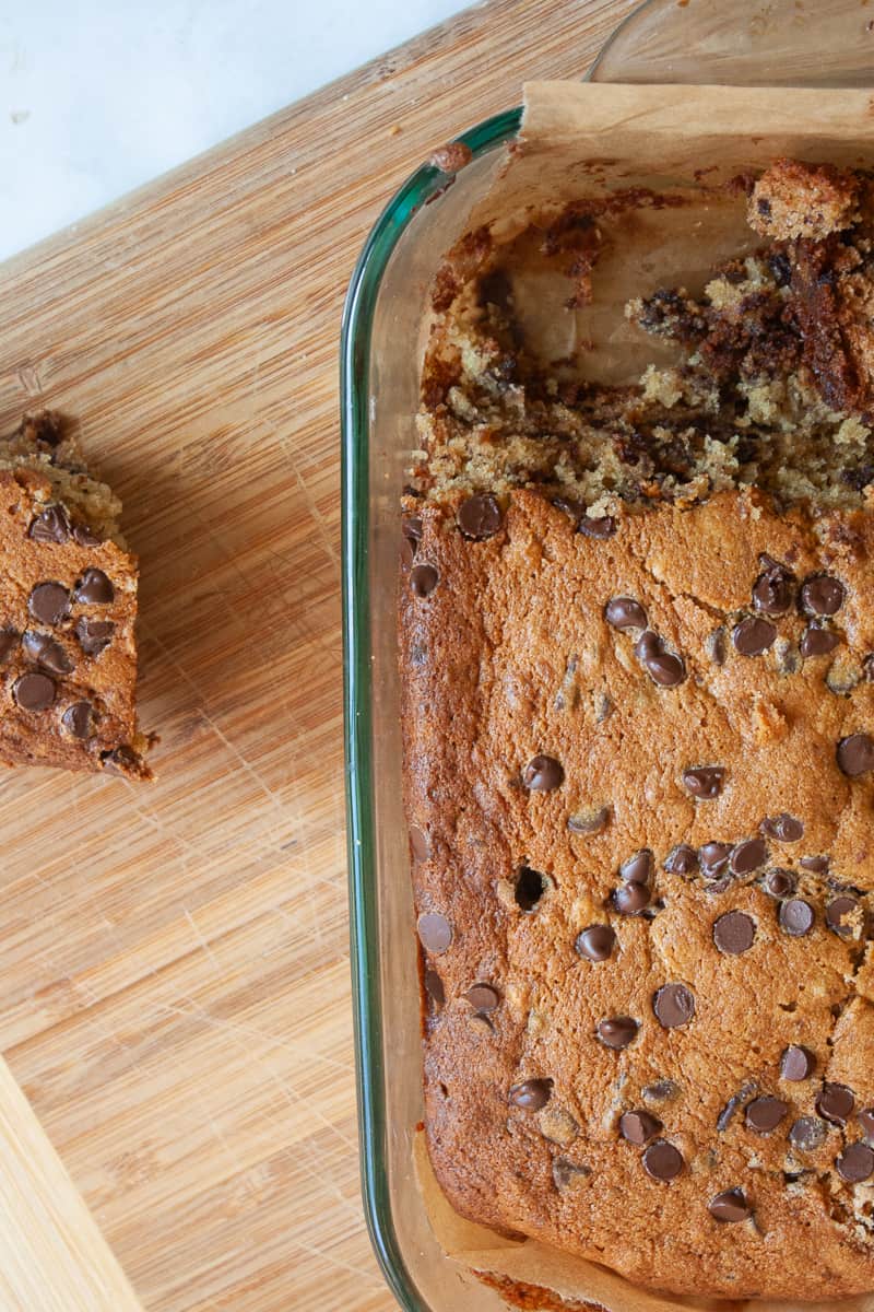 Gluten free banana chocolate chip cake in the pan, with a piece removed.