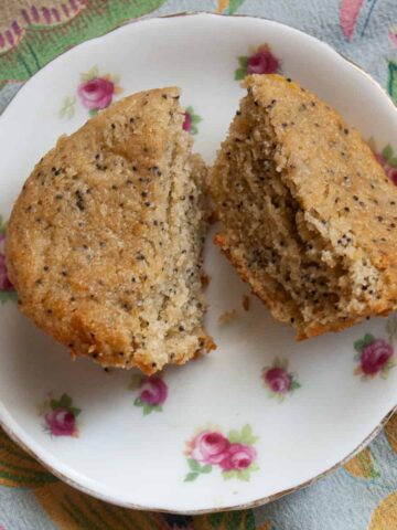 A lemon poppy seed muffin is cut in half on a plate to show its crumb.