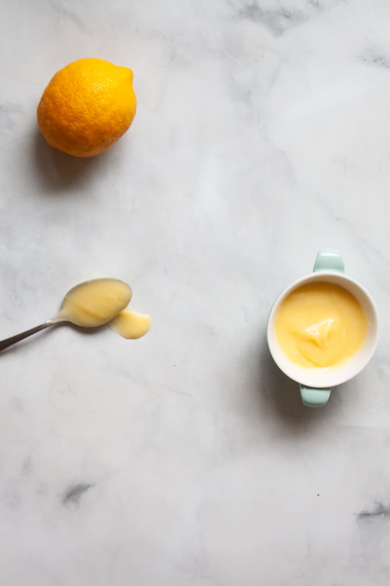 A lemon, spoon, and dish full of honey lemon curd.