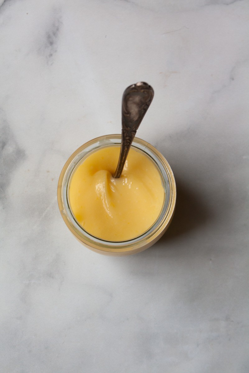 A spoon rests in a jar of lemon curd.