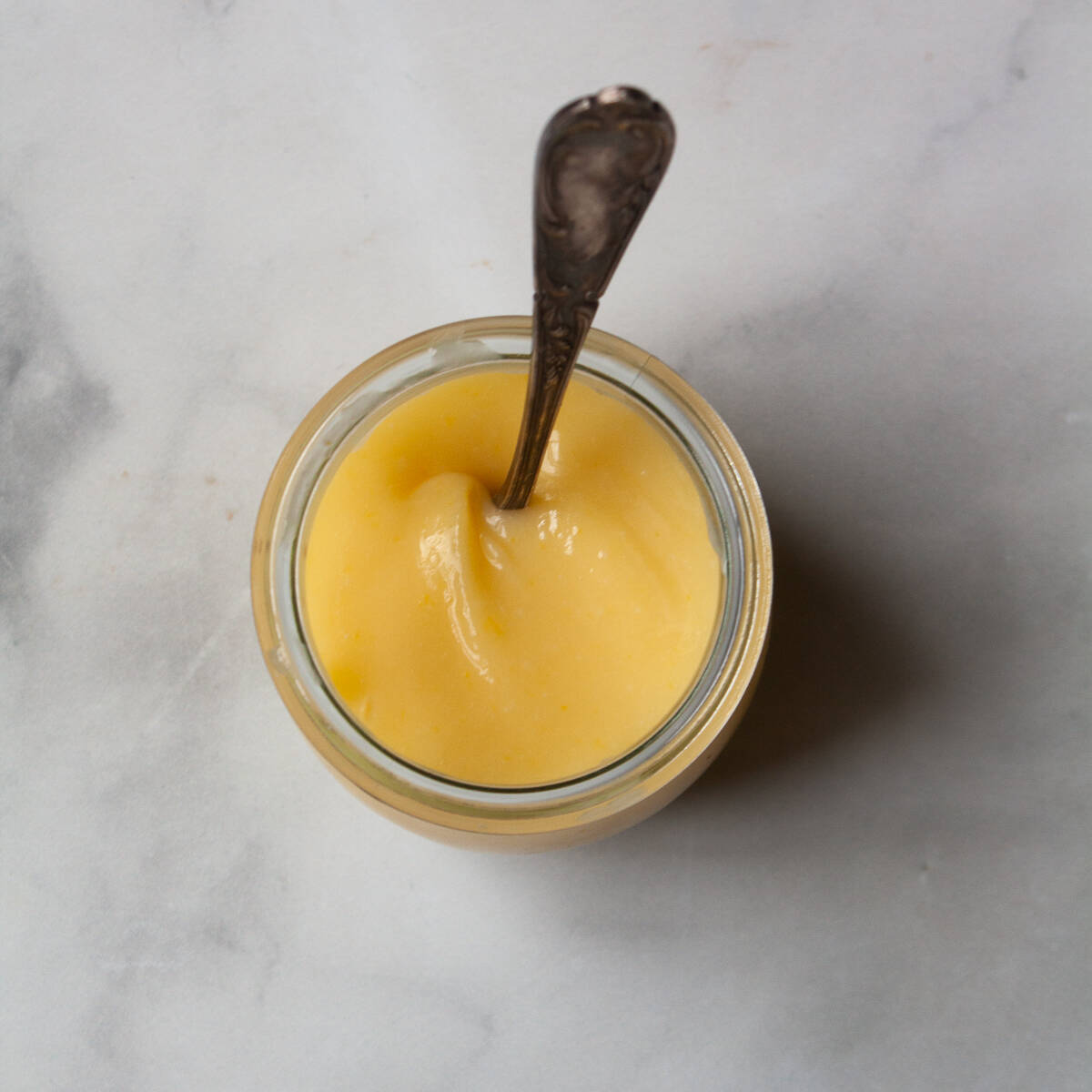 A spoon rests in a jar of lemon curd.