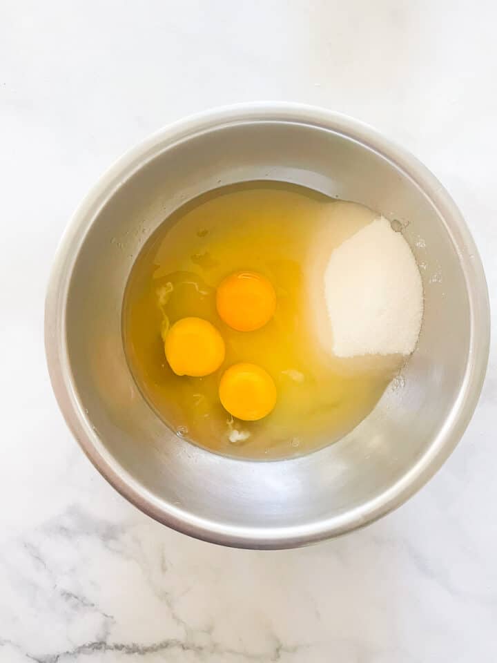 The egg yolks and sugar are combined in a stainless steel bowl.