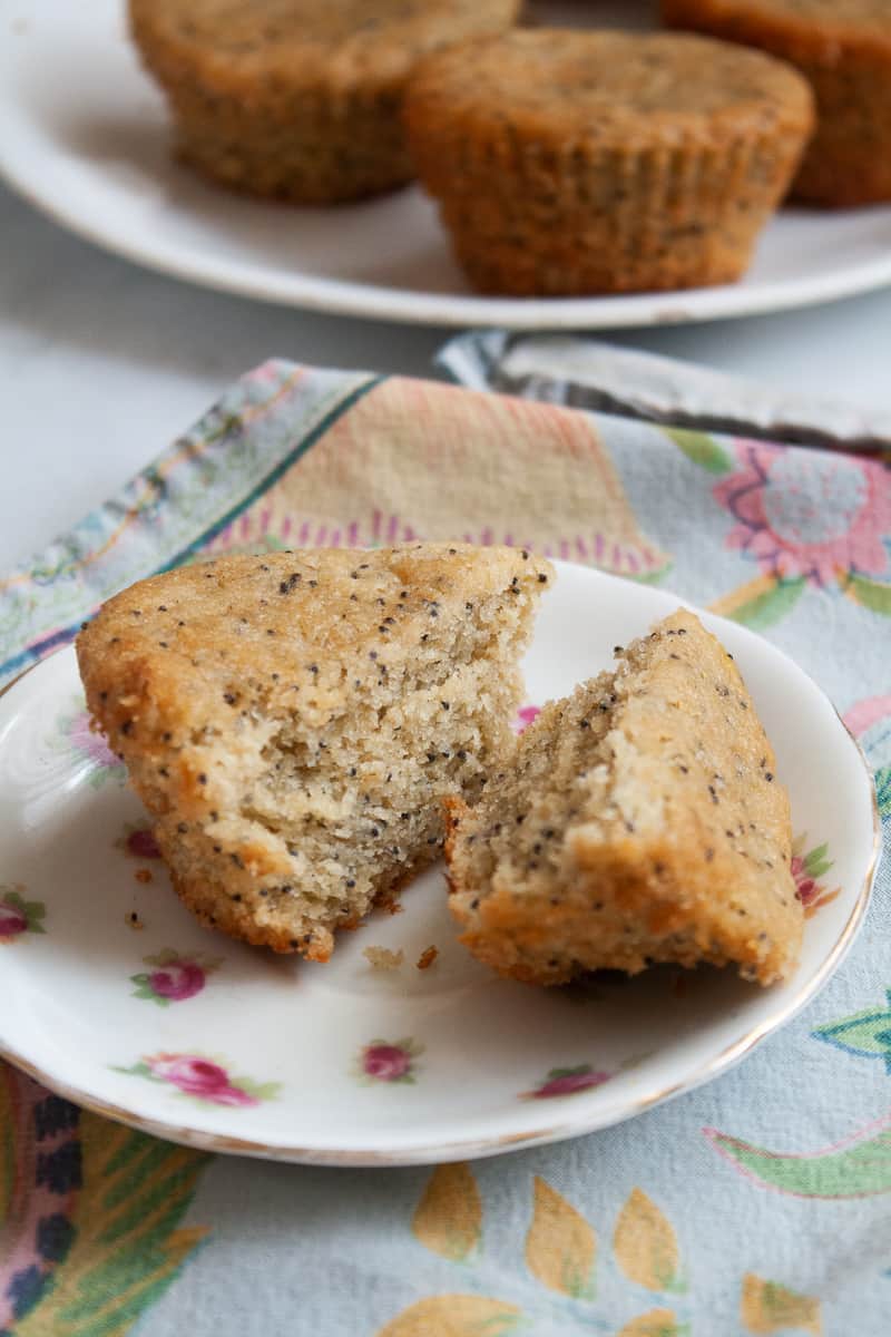 A gluten free lemon poppyseed muffin is cut in half on a plate with more muffins in the background.