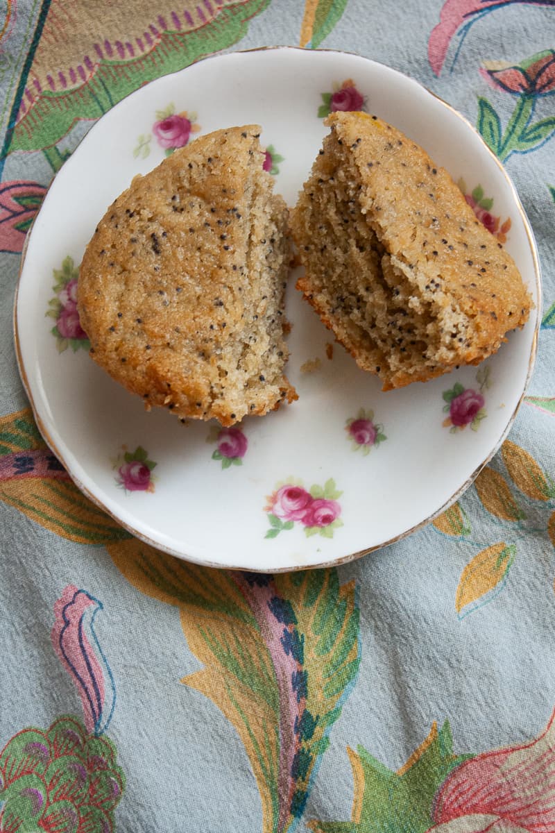 A gluten free lemon poppy seed muffin is cut in half on a plate.