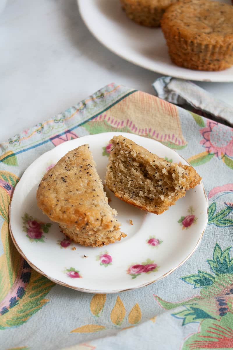 A plate of lemon poppy seed muffins with a halved muffin on a plate in front of it.