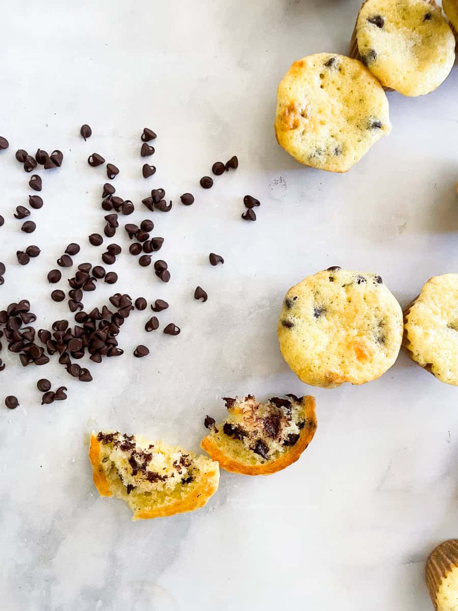 Mini chocolate chips are tossed next to mini chocolate chip muffins.