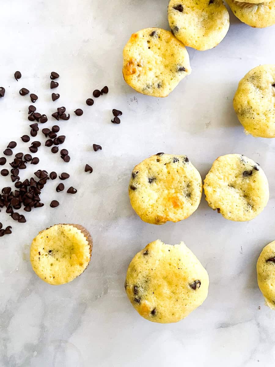 A handful of mini chocolate chips next to mini chocolate chip muffins.