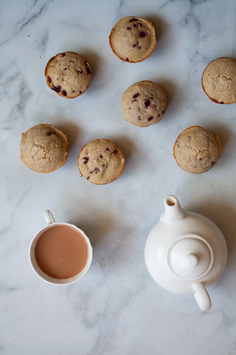 Oatmeal raspberry muffins are scattered on a white background with a pot of tea and a cup of tea.