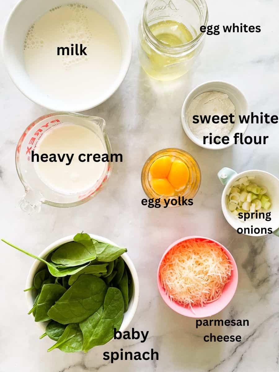 The ingredients for gluten free souffle are shown labeled and portioned out: egg whites, egg yolks, sweet white rice flour, milk, cream, spinach, parmesan cheese, spring onions.