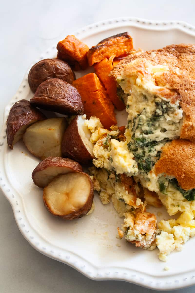 A white plate with a serving of gluten free souffle plus roasted potatoes and sweet potatoes.
