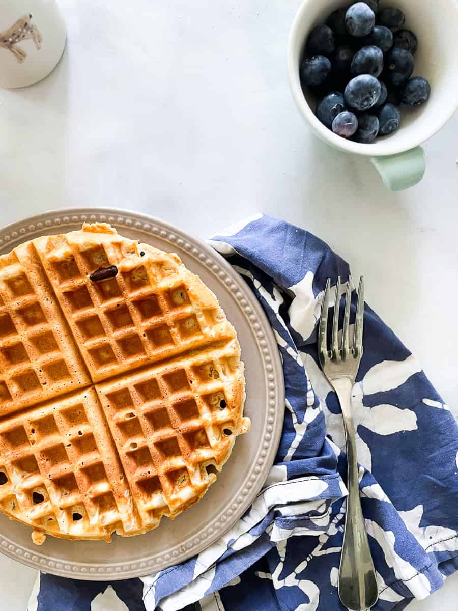 A gluten free waffle on a plate with a blue napkin and fork next to it.