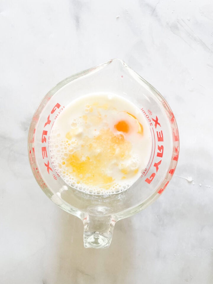 Egg and melted butter are added to a glass measuring cup of milk.