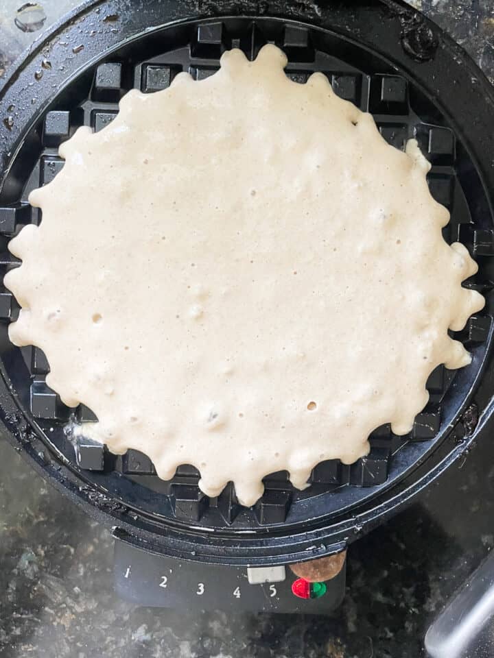 A waffle cooks on a waffle maker.