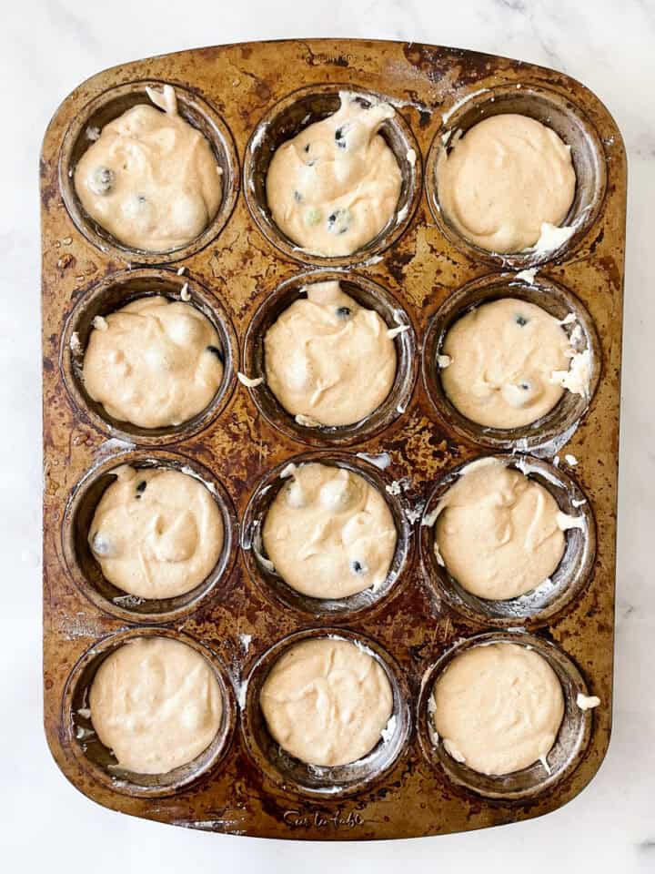 A muffin tin holds 12 cups full of oat flour blueberry muffin batter.