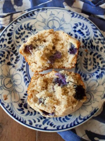 An oat flour blueberry muffin is cut in half on a blue and white plate.