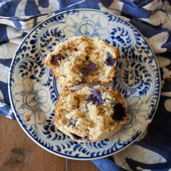 An oat flour blueberry muffin is cut in half on a blue and white plate.