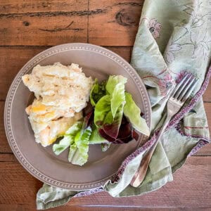 A plate of cauliflower cheese casserole with a salad on a wooden table.