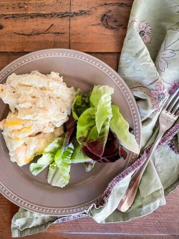 A plate of cauliflower cheese casserole with a salad on a wooden table.