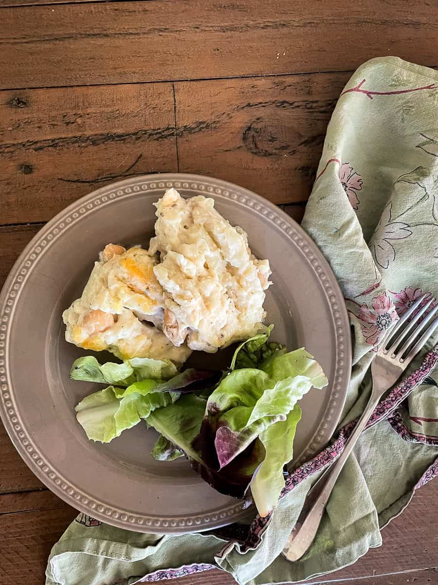 A plate of cauliflower cheese casserole with a salad on a wooden table with a green napkin and fork.