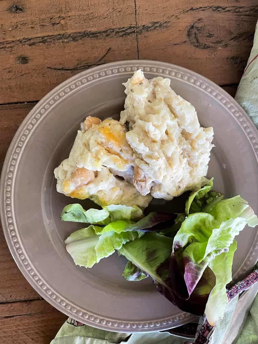 A serving of cauliflower cheese casserole on a plate with a salad.