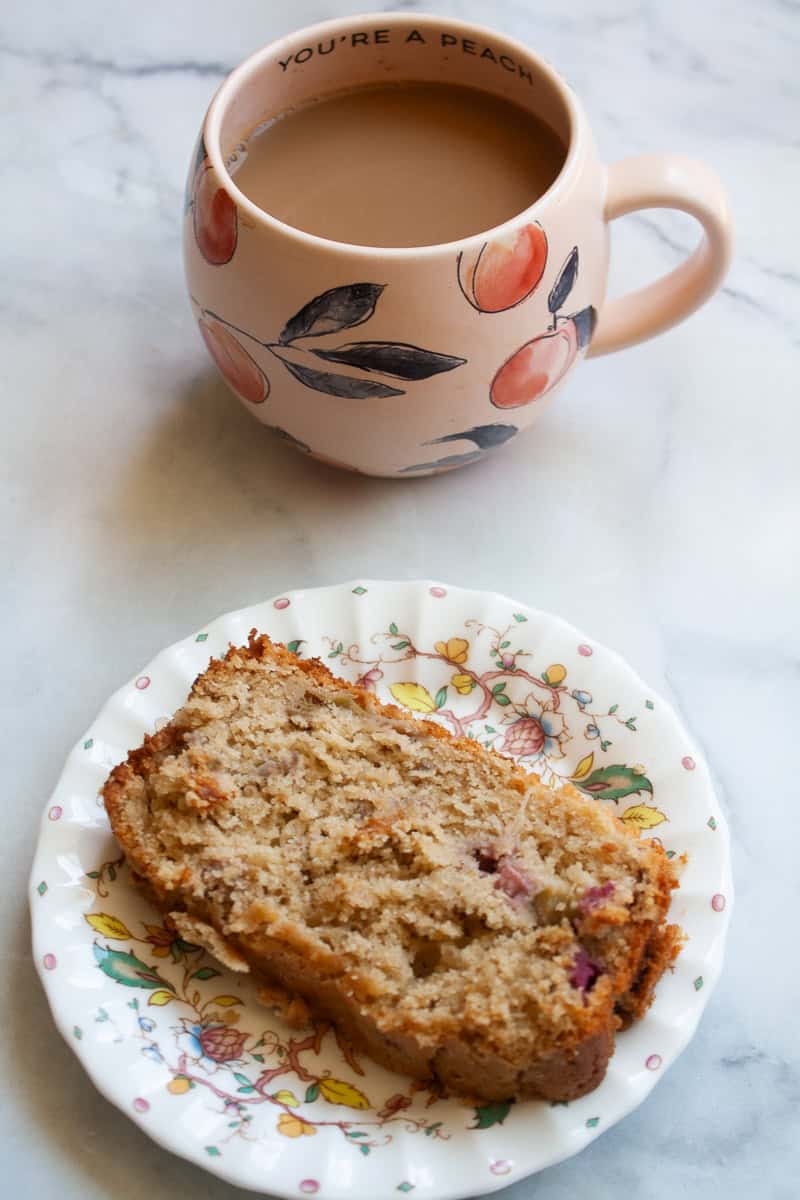 A cup of coffee in a pink cup next to a slice of rhubarb bread on a plate.