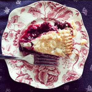 A piece of black raspberry pie is served on a flowered plate with a fork.