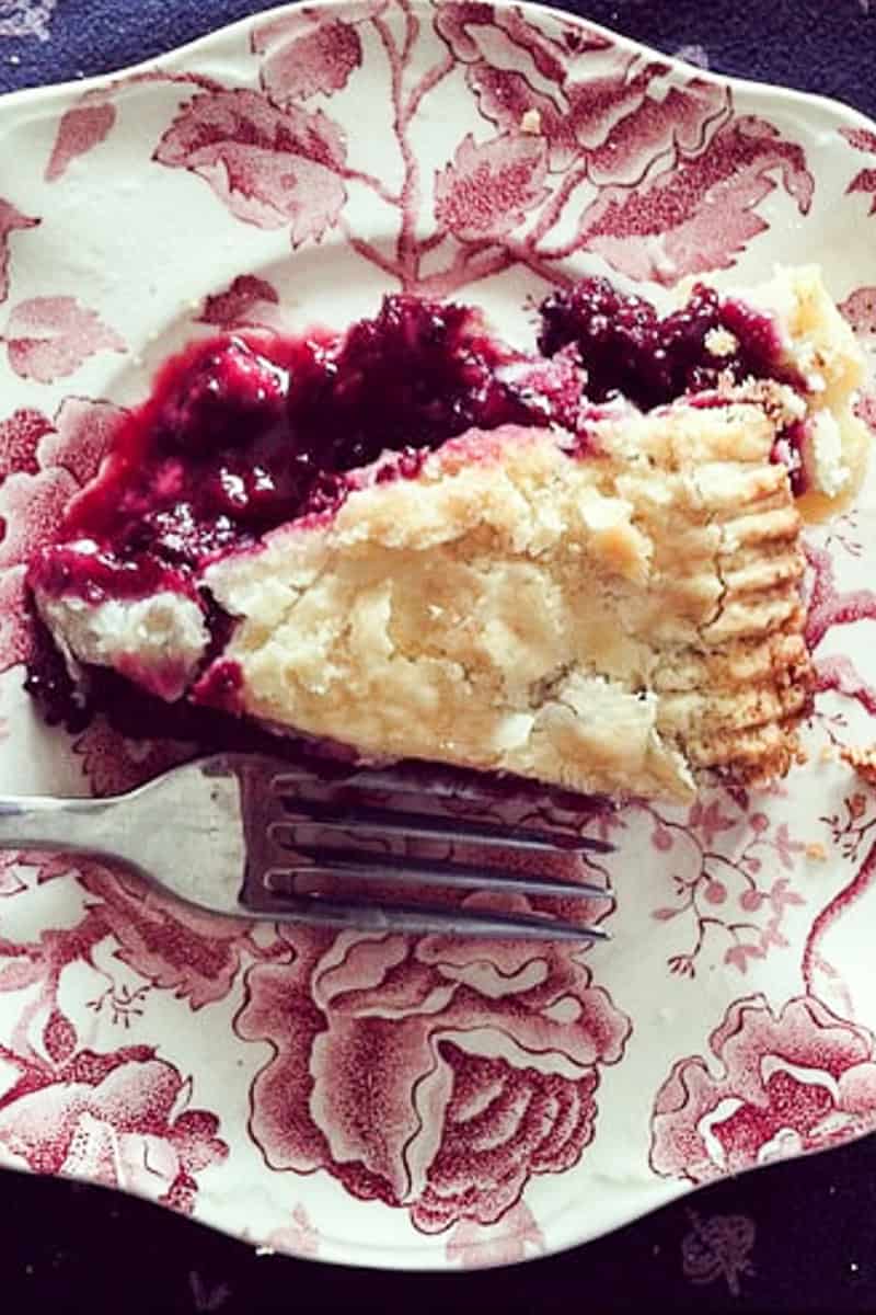 A piece of black raspberry pie is served on a flowered plate with a fork.