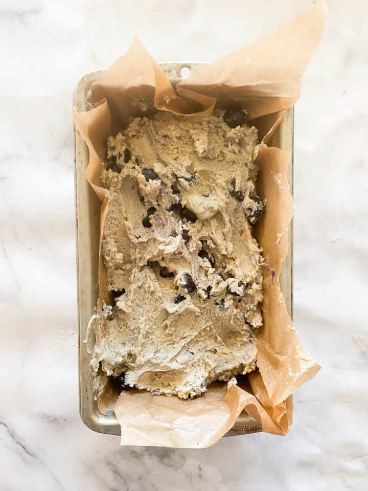 The batter for blueberry bread is spread in a metal loaf pan lined with parchment paper.