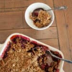 A bowl of cherry crisp with a spoon next to a pan of crisp.