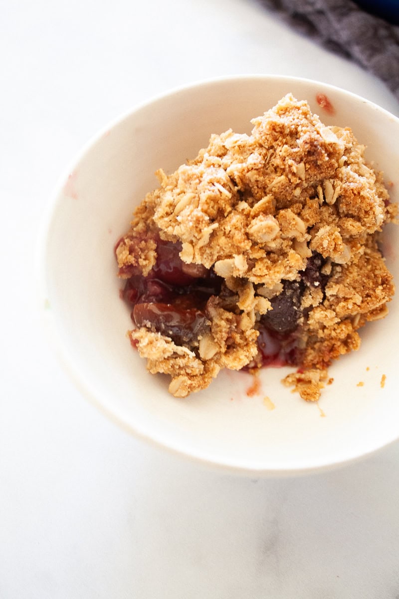 A portion of gluten free cherry crisp in a white bowl.