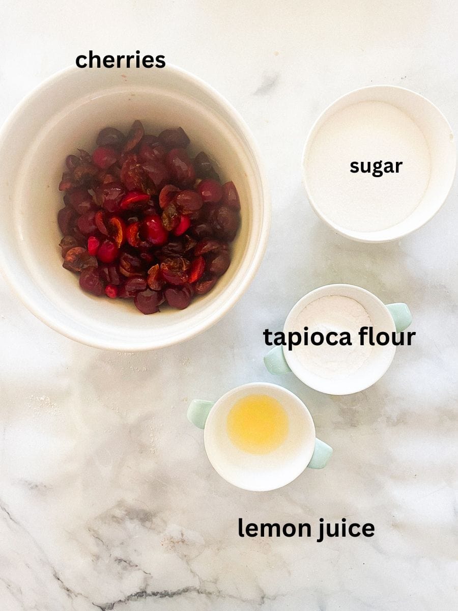 The ingredients for cherry crisp filling are portioned and labeled: cherries, tapioca flour, lemon juice, sugar.